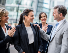 A woman in a suit being congratulated by colleagues